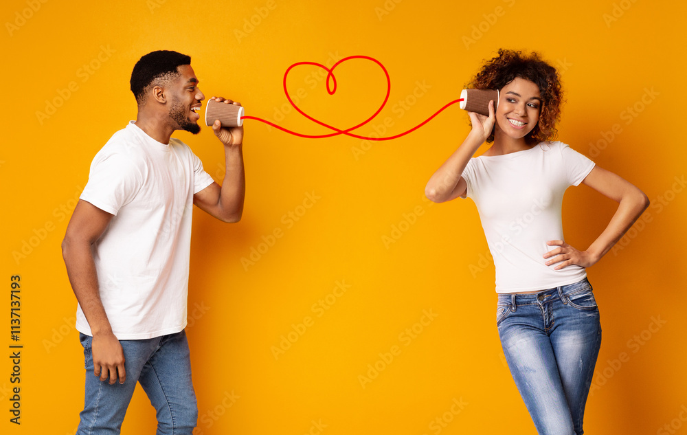 © Prostock-studio - African-american man singing love song to his girlfriend via tin phone, orange studio background, copy space