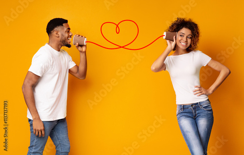 African-american man singing love song to his girlfriend via tin phone, orange studio background, copy space photo