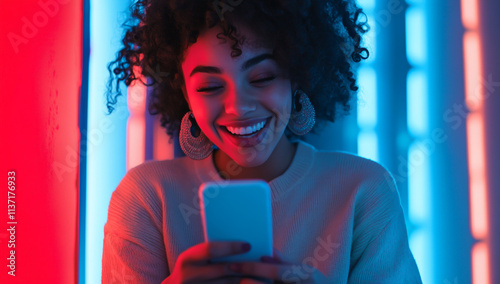 An excited young woman looking at her phone and smiling, illuminated by blue and red lights in the background