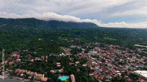 Wide, slow aerial shot over a town near Taal Volcano on a cloudy day, revealing a mix of village homes and a resort surrounded by lush palm trees. Lemery, Batangas, Philippines. photo