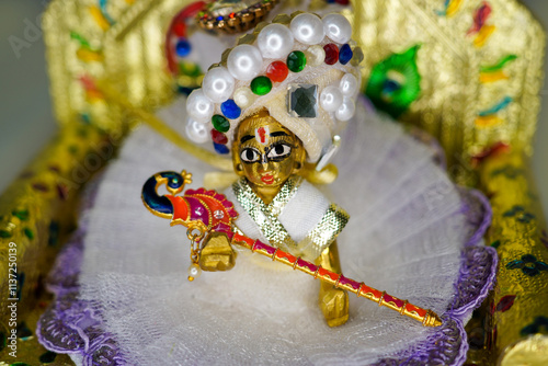 Close up on statue of Hindu God Lord Krishna also known as Bal Gopal sitting on his throne on Janmashtami festival. Selective focus on lord Krishna on White background.