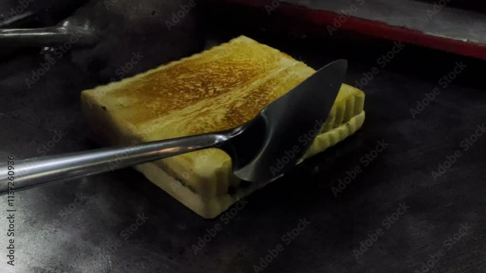 A roadside toast vendor is baking bread in a non-stick steel toast pan. “Roti Bakar Gerobakan” or 
