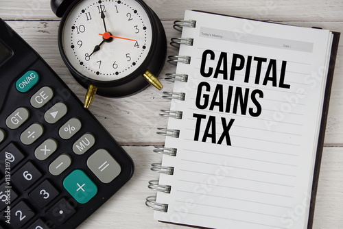 Capital Gains Tax text on notepad with alarm clock and calculator on wooden background