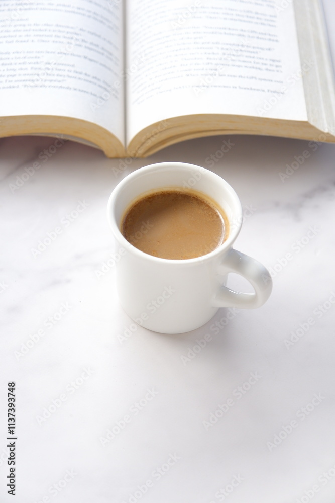 テーブルの上の開いた本（洋書）と、コーヒーの入ったコーヒーカップで、コーヒーを飲みながらゆっくりと読書を楽しんでいるイメージ

