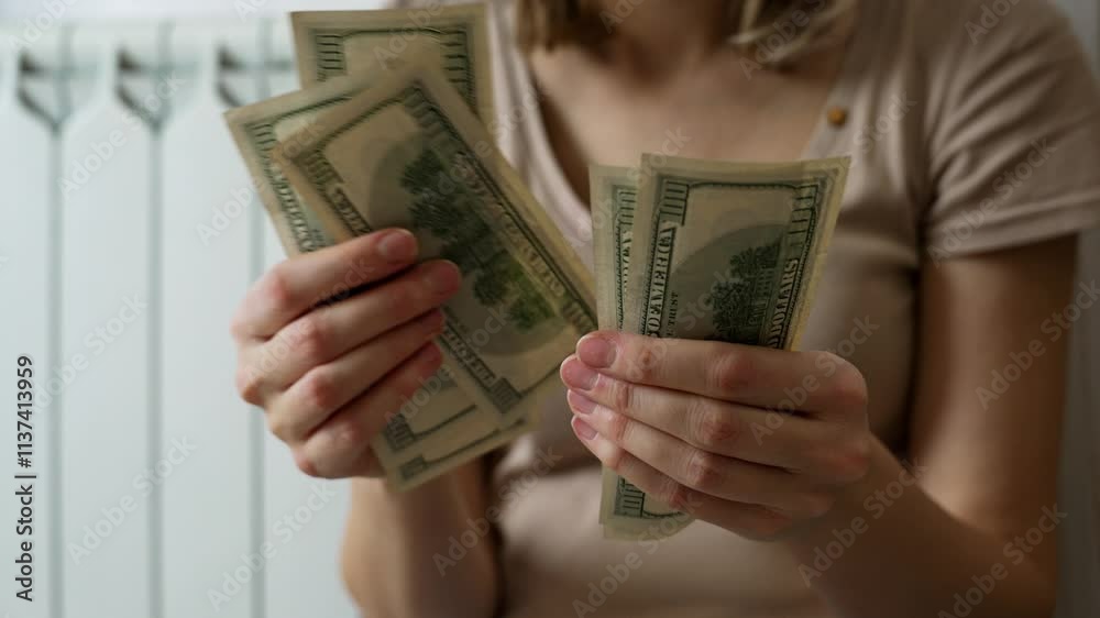 A woman counts her cash nervously while seated next to a heater. She faces escalating utility bills and increased prices during an ongoing energy crisis, highlighting financial stress.