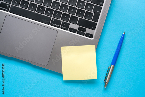 Top view of blank post-it stuck on laptop on blue table