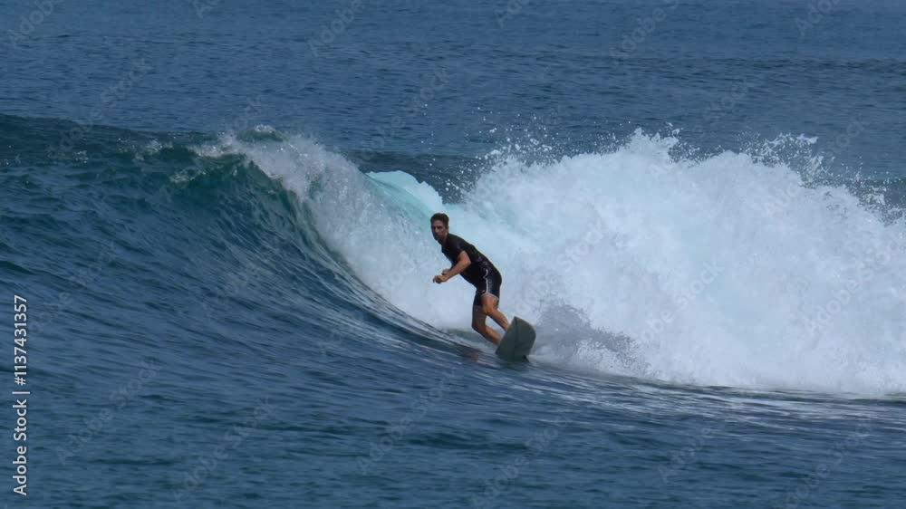 Young male adult surfs in the blue ocean at sunny day Young male adult surfs in the blue ocean at sunny day