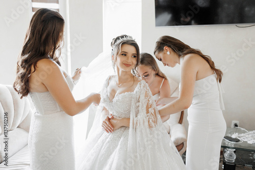 A bride is getting ready for her wedding with her bridesmaids. The bride is wearing a white dress and is sitting on a couch