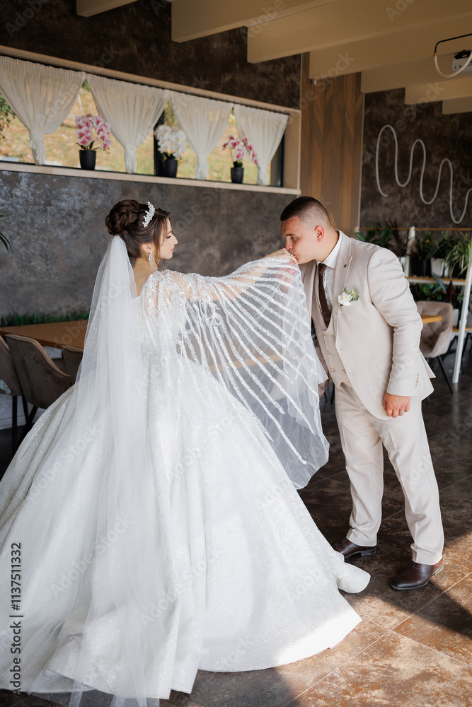 Fototapeta premium A bride and groom are standing in a room with a white curtain behind them. The bride is wearing a white dress and a veil, while the groom is wearing a suit. They are both smiling