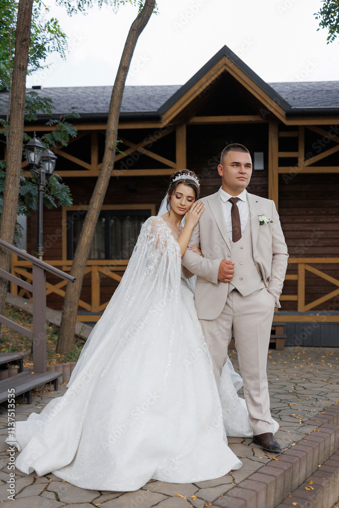 Fototapeta premium A bride and groom are standing outside a house, with the bride wearing a white dress and the groom wearing a suit