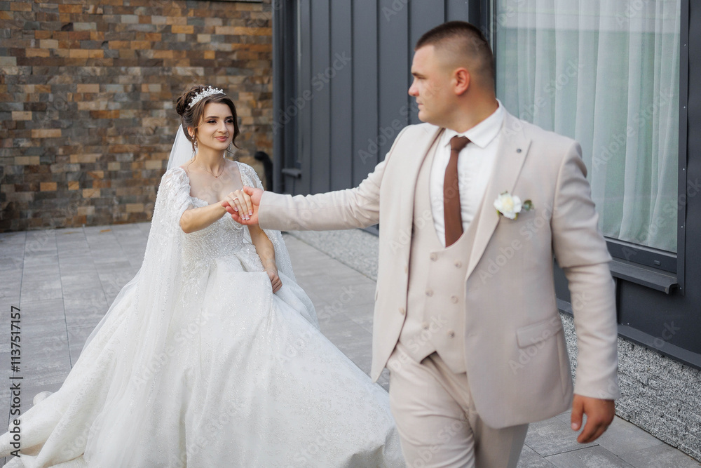 Fototapeta premium A bride and groom are walking down a street, the bride is wearing a white dress and the groom is wearing a suit
