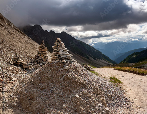 A pile of gravel, sand, and stones stacked beside a rocky mountain trail under cloudy skies photo