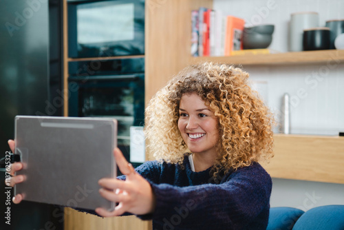 Smiling young woman taking selfie with tablet PC at home photo