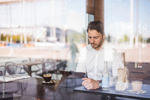 Businessman behind windowpane using tablet in a cafe photo