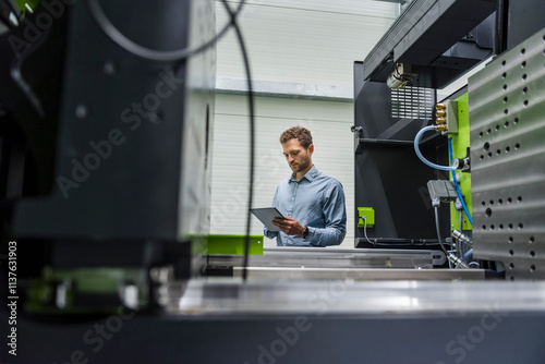 Businessman in high tech company controlling manufacturing machines, using digital tablet