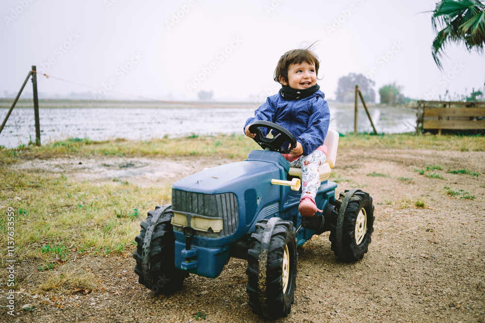 Baby girl driving a toy tractor next to the rice fields Baby girl driving a toy tractor next to the rice fields
