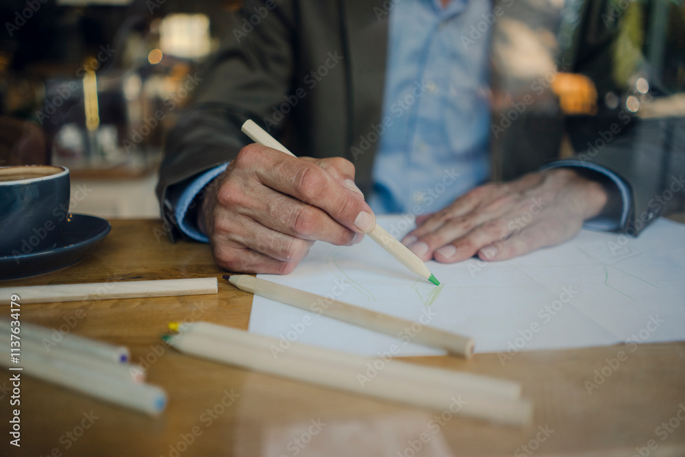 Mature businessman sitting in coffee shop, drawing on paper Mature businessman sitting in coffee shop, drawing on paper