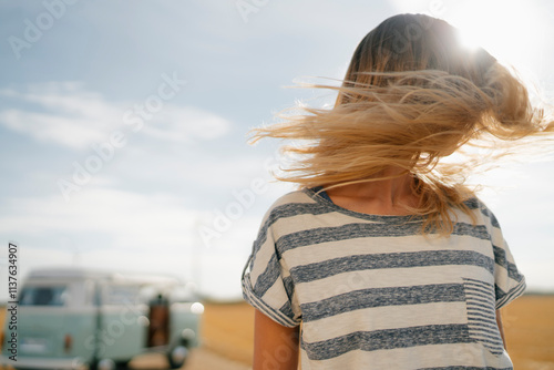 Blong young woman at camper van in rural landscape shaking her hair photo