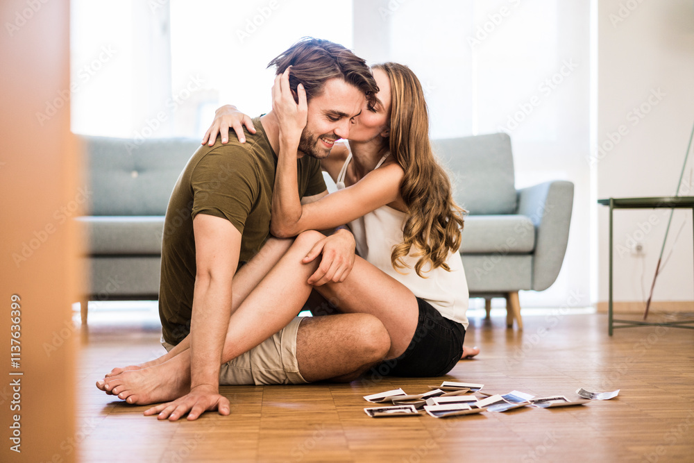 Happy affectionate couple sitting at home with photographies on the floor Happy affectionate couple sitting at home with photographies on the floor