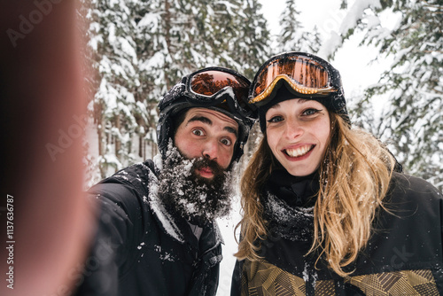 Selfie of happy couple in skiwear in winter forest photo