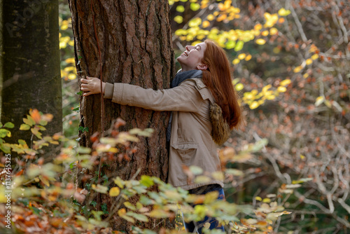 Happy teenage girl hugging tree trunk in autumnal forest