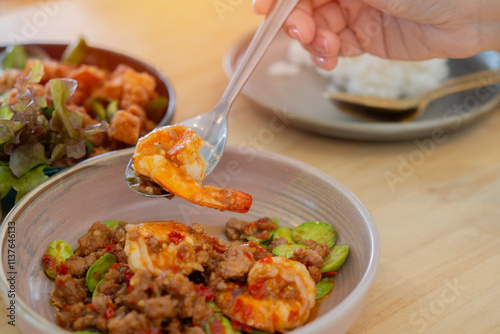 A young woman's hand uses a spoon to scoop up a menu of stir-fried Sator with shrimp photo