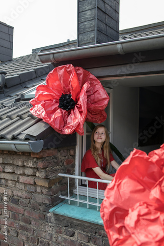Smiling girl with oversized redc artifical flower looking out of window