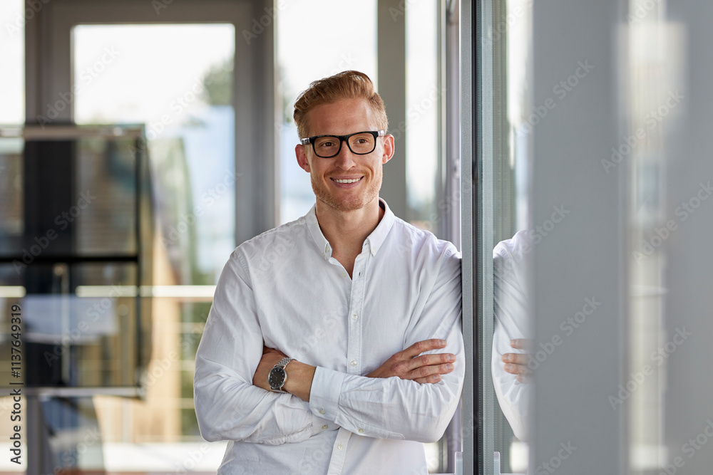Portrait of smiling businessman in office leaning against window Portrait of smiling businessman in office leaning against window