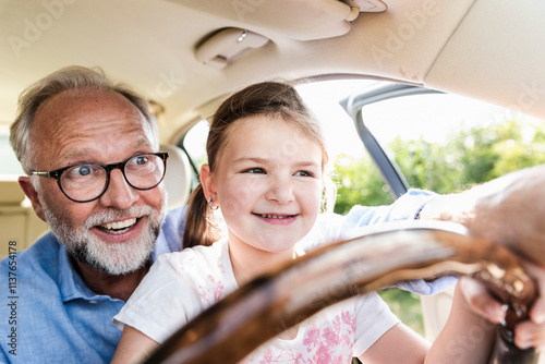 Little girl sitting on lap of grandfather, pretending to steer the car