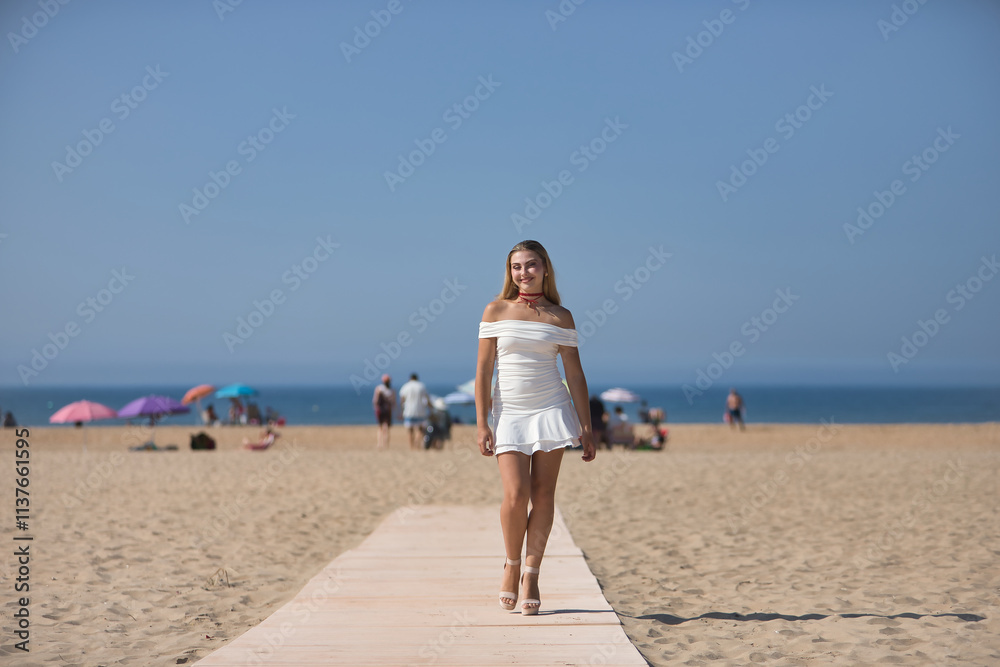 Young, beautiful, blonde woman in white dress and heels, parading as a model on a wooden walkway on the beach. Concept beauty, fashion, trend, femininity. Young, beautiful, blonde woman in white dress and heels, parading as a model on a wooden walkway on the beach. Concept beauty, fashion, trend, femininity.