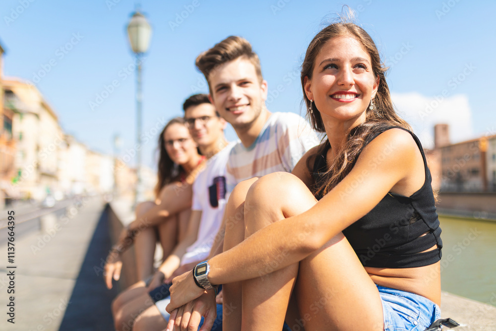 © Westend61 - Italy, Pisa, group of four happy friends sitting on a wall along Arno river