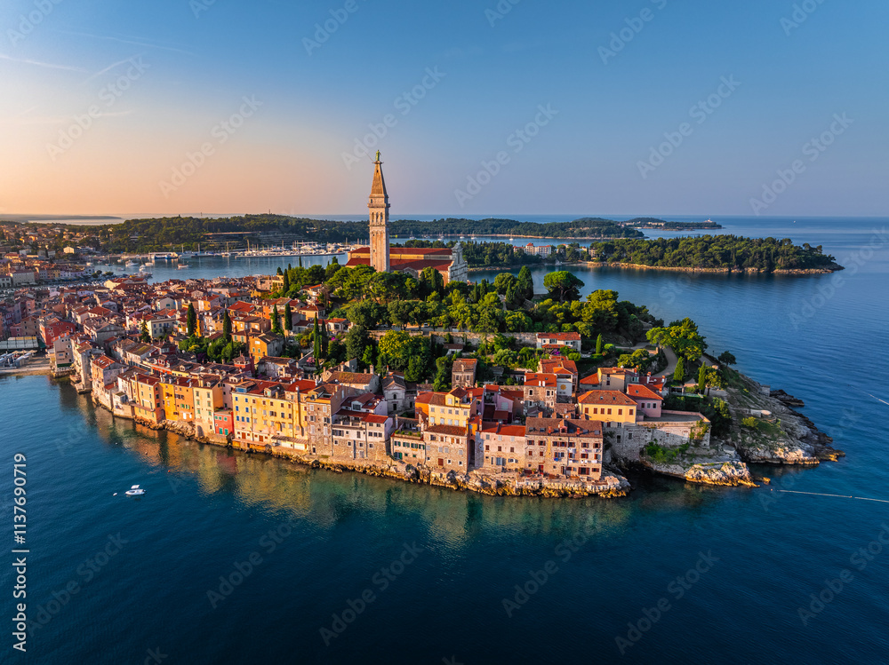 Rovinj, Croatia - Aerial view of the old town of Rovinj with Church of St. Euphemia at sunrise on a summer morning in Istria, Croatia. Golden sky and red rooftops by the Adriatic sea