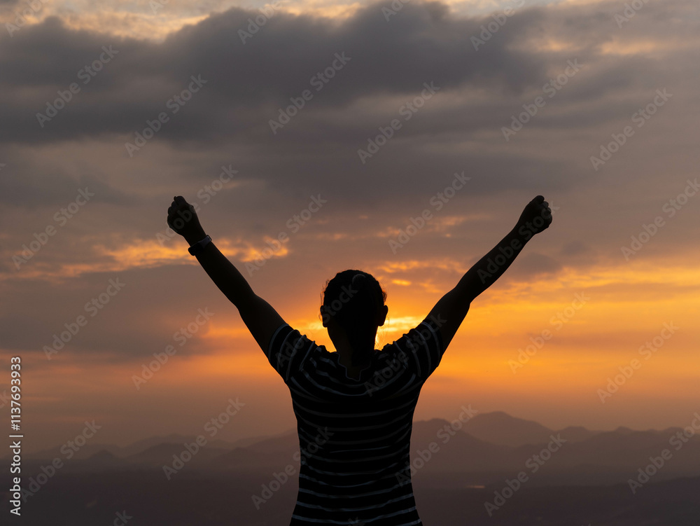 Fototapeta premium Silhouette of a young woman relaxing in the summer sunset outdoors. A dreamy young woman looking hopeful at the horizon.