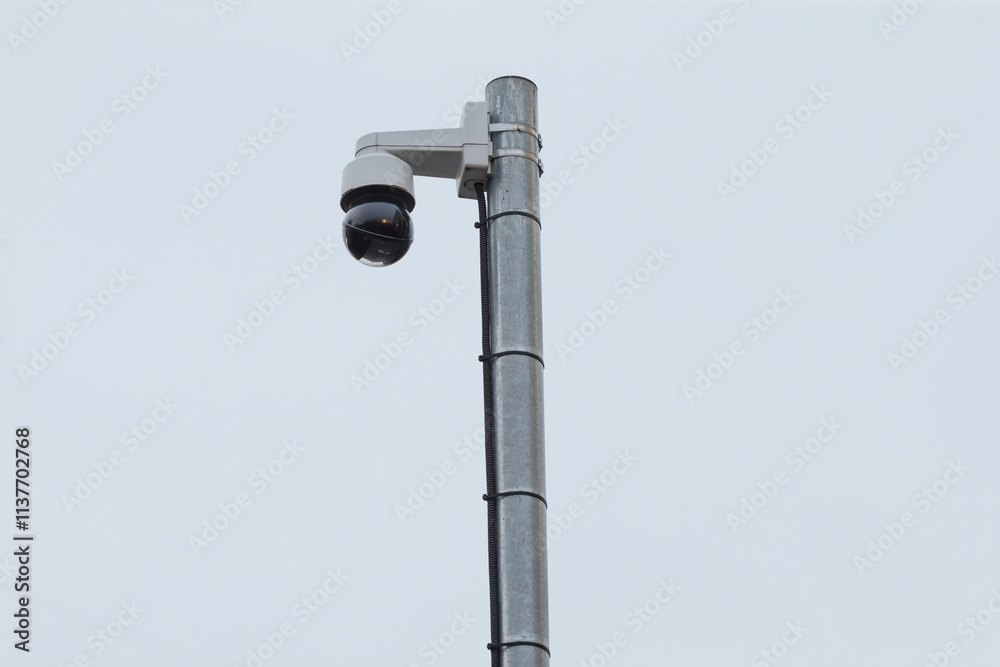 A surveillance security camera is positioned on top of a tall pole, diligently monitoring the area below for safety and security purposes A surveillance security camera is positioned on top of a tall pole, diligently monitoring the area below for safety and security purposes