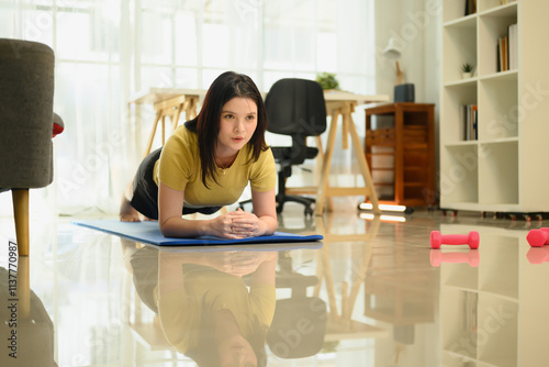 Determined young woman doing plank exercises on mat during home fitness session