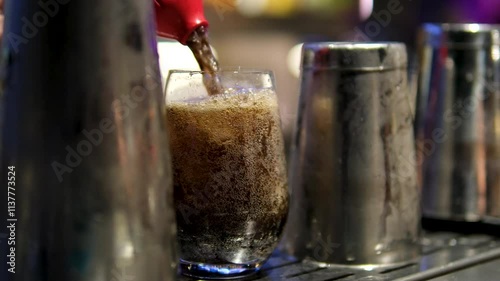 Pouring Cola with ice cubes close-up. Cola with Ice and bubbles in glass. Coke Soda closeup. Food background. Rotate glass of Cola fizzy drink over brown background. Slow motion