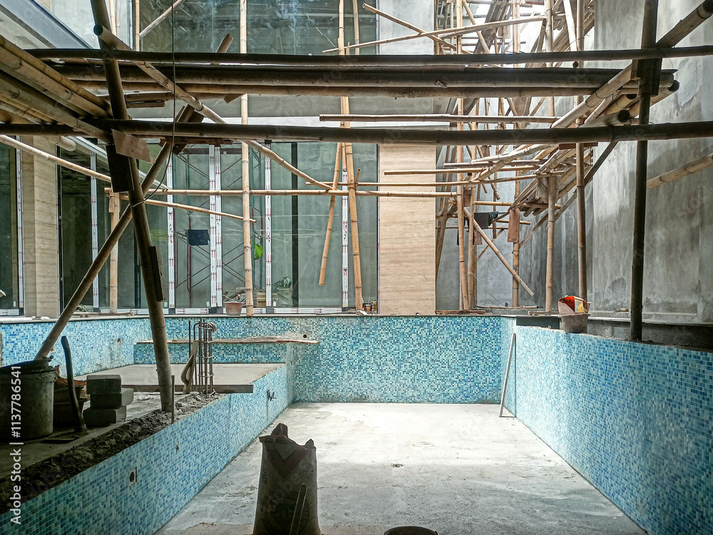 Obraz premium Workers are building a swimming pool in the middle of a building using bamboo scaffolding.