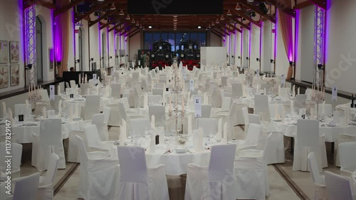 Elegant banquet hall with white table settings, candles, and covered chairs, featuring a railway theme with vintage trains in the background under soft purple lighting.
