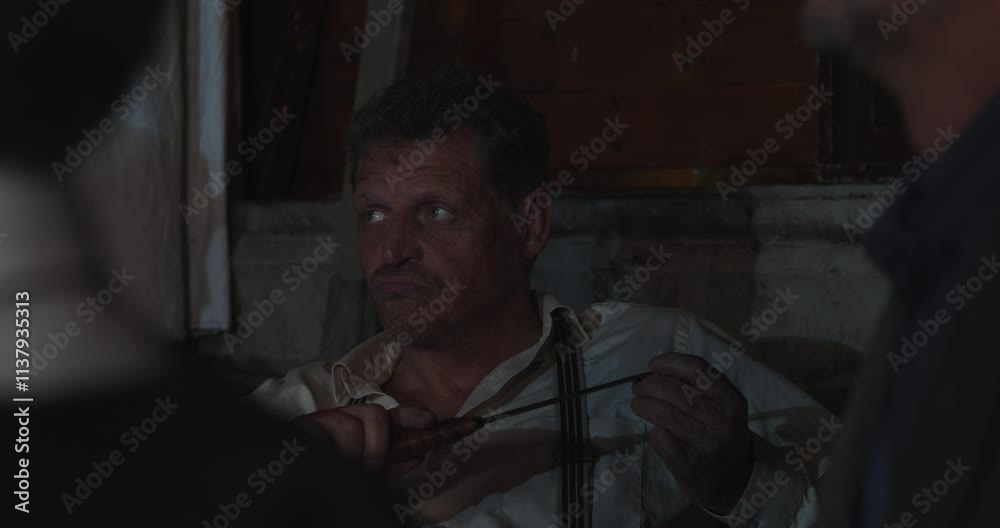 An intimidating gangster with scars in face plays with a knife while asking a question to another person An intimidating gangster with scars in face plays with a knife while asking a question to another person