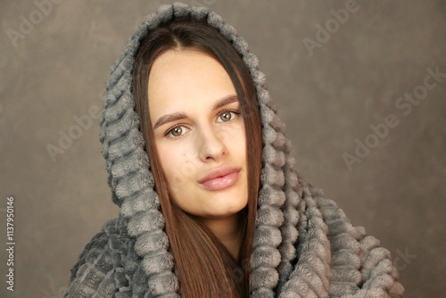 
A young woman on a gray background. Portrait of a woman wrapped in a blanket on a gray background