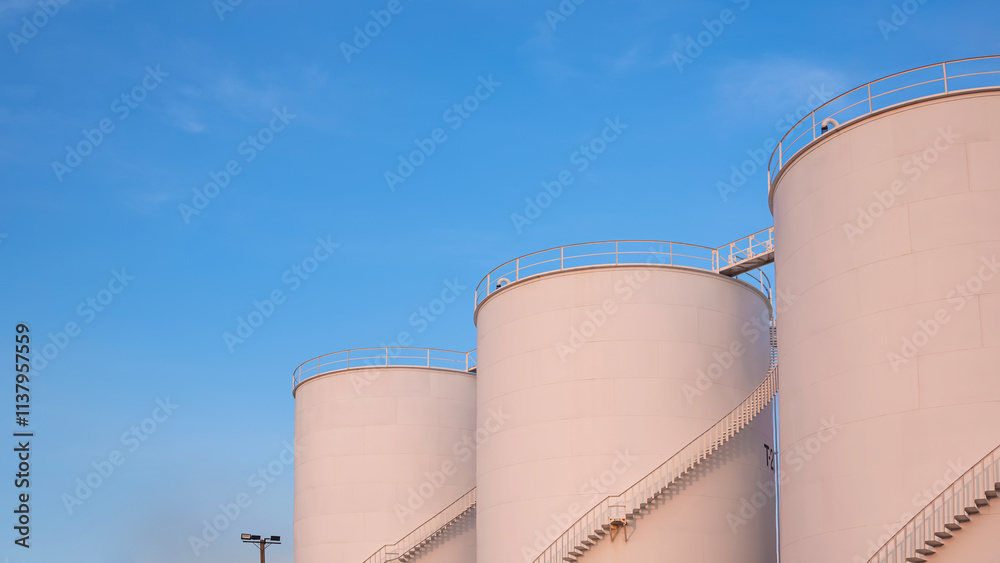 Three storage fuel tanks in petrochemical refinery area with orange sunlight on surface against blue evening sky background, low angle view with copy space Three storage fuel tanks in petrochemical refinery area with orange sunlight on surface against blue evening sky background, low angle view with copy space