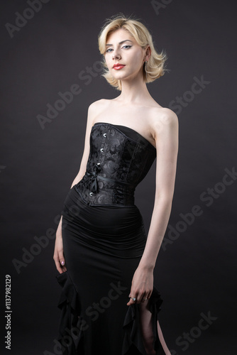 Expressive young blonde under a bob in the studio. In a black corset and dress.