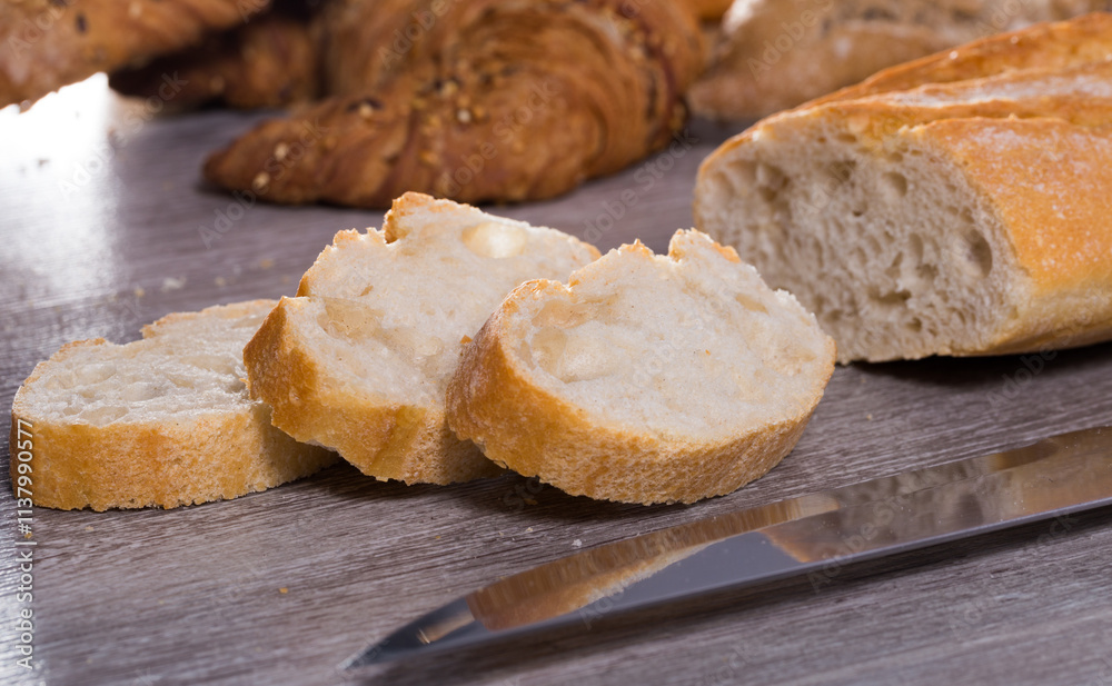 Slices of wheaten bread and knife on wooden surface Slices of wheaten bread and knife on wooden surface