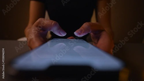 Top view of unrecognizable woman using typing smartphone in dark room, browsing online content with illuminated screen. Female searching web while reading news and blog posts online, slow motion.