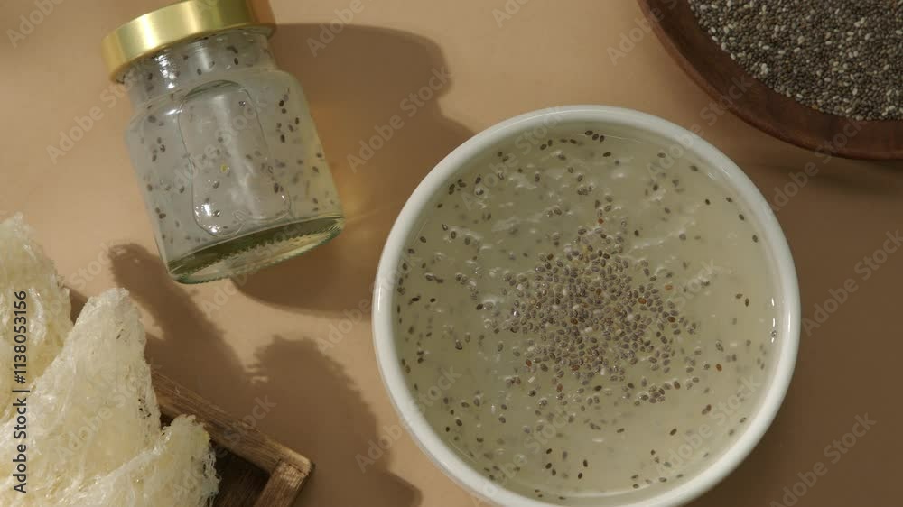 A mockup of a chia seed bird's nest bowl, a healthy dish, is displayed on a brown surface with a tray of raw swallow nests, chia seeds, and rock sugar, at a top-down angle from left to right. A mockup of a chia seed bird's nest bowl, a healthy dish, is displayed on a brown surface with a tray of raw swallow nests, chia seeds, and rock sugar, at a top-down angle from left to right.