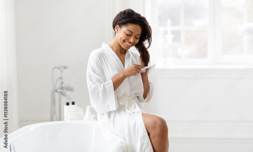 A pretty African American woman enjoys her skincare routine in a bright, minimalist bathroom. She sits on the edge of a bathtub, smiling while combing her hair. Natural light fills the space. A pretty African American woman enjoys her skincare routine in a bright, minimalist bathroom. She sits on the edge of a bathtub, smiling while combing her hair. Natural light fills the space.