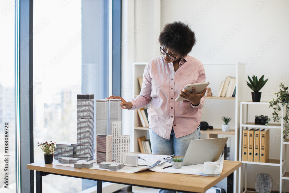 African American woman architect mid-30s develops modern city project using digital tablet office environment.