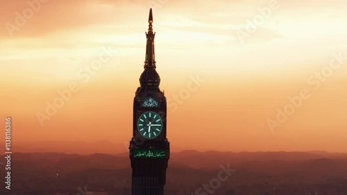 Aerial view of the Abraj Al Bait Clock Tower in Mecca, Saudi Arabia, silhouetted against a golden sunset with distant mountains in the background