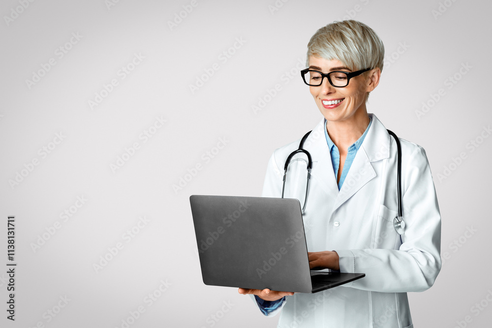 Search on internet and view reviews. Smiling woman doctor typing on laptop isolated on light background, studio shot Search on internet and view reviews. Smiling woman doctor typing on laptop isolated on light background, studio shot
