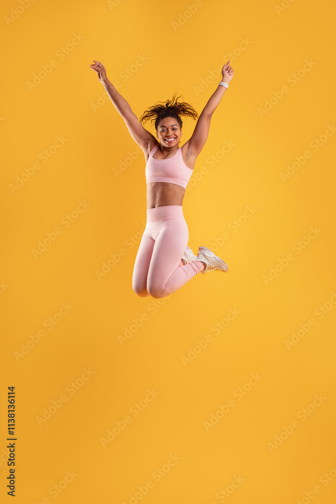 A young woman in a pink athletic outfit joyfully jumps with her arms raised, showcasing excitement and energy. The vivid yellow background enhances her dynamic movements during the activity. A young woman in a pink athletic outfit joyfully jumps with her arms raised, showcasing excitement and energy. The vivid yellow background enhances her dynamic movements during the activity.